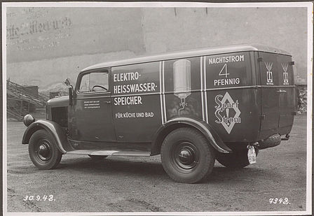 Das Bild zeigt einen kleinen Lieferwagen. Auf der Seite befinden sich die Aufschriften „Elektro-Heisswasser-Speicher für Küche und Bad“ sowie „Nachtstrom 4 Pfennig. Spart Strom!“ Es ist ein Heißwasserboiler abgebildet. 