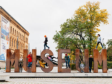 Auf der Wortskulptur "Museum" auf dem Vorplatz des Deutschen Technikmuseums haben sich Kinder und Erwachsene in und af die Buchstaben gesetzt.