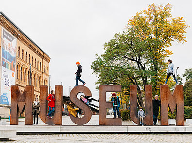 Auf der Wortskulptur "Museum" auf dem Vorplatz des Deutschen Technikmuseums haben sich Kinder und Erwachsene in und af die Buchstaben gesetzt.