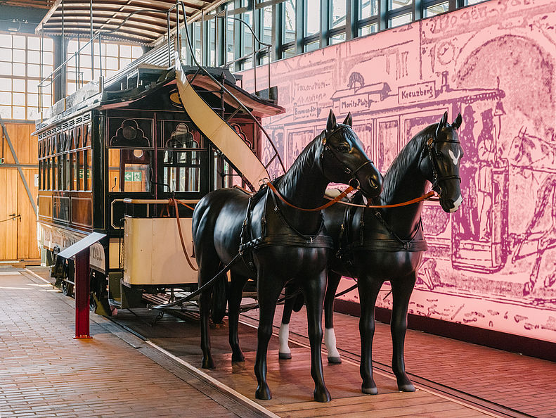 Ein historischer Pferdebahnwagen mit zwei davor angespannten Pferde-Attrappen.