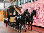 Ein historischer Pferdebahnwagen mit zwei davor angespannten Pferde-Attrappen.