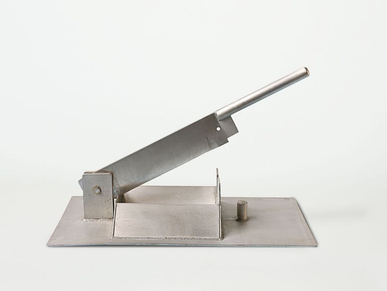 Der Stierhodenschneider wurde um 1950 von der Firma Schering gebaut. Es handelt sich um eine besonders stabile Schlagmesserklinge, die auf eine Metallplatte montiert ist, und mit einem Metallgriff an der Seite heruntergedrückt wird.