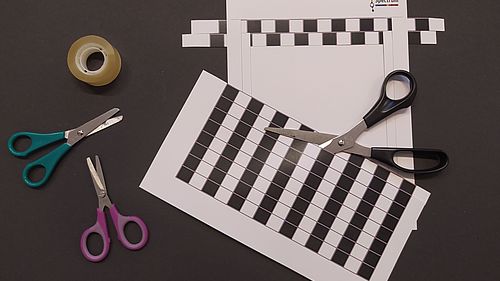 zwei Scheren und Klebeband, daneben die Vorlage aus Papier zum Basteln der Täuschung.