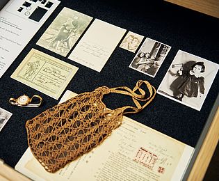 View into an open drawer. Family photographs can be seen along with a wristwatch and a crocheted ladies handbag. 