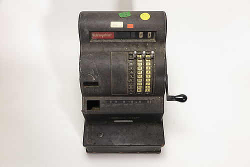 Registrierkasse aus den 1930er Jahren mit vier farbigen Aufklebern der KuA. Die Aufkleber tragen Zahlen und Buchstaben.