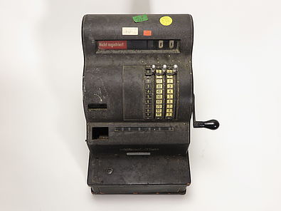 Cash register from the 1930s with four colored KuA stickers. The stickers have different numbers and letters on them.