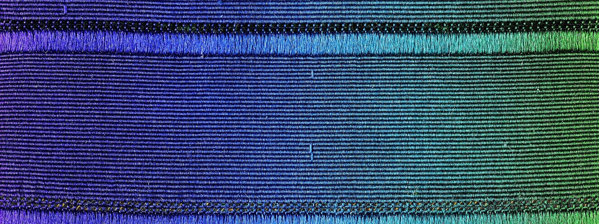 Detailaufnahme eines Textilbands mit einem Farbverlauf von Violett über Blau zu Grün. 