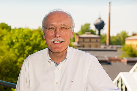 Das Foto zeigt Dirk Böndel, der 16 Jahre lang Direktor des Museums war, und nun in den Ruhestand geht. Ein Mann mit grauen Haaren und Schnurrbart lächelt in die Kamera, im Hintergrund sieht man den Museumspark.