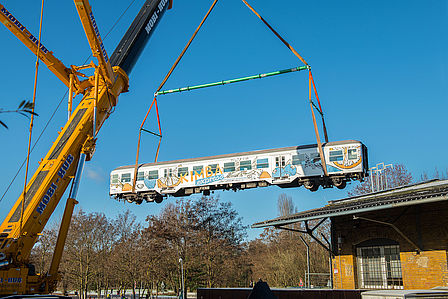 Ein Eisenbahnwagen hängt an einem Kran und schwebt in der Luft