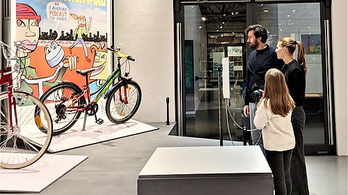 Ein Mann, eine Frau und ein Kind stehen an einer Hörstation in der Sonderausstellung "Rückenwind".