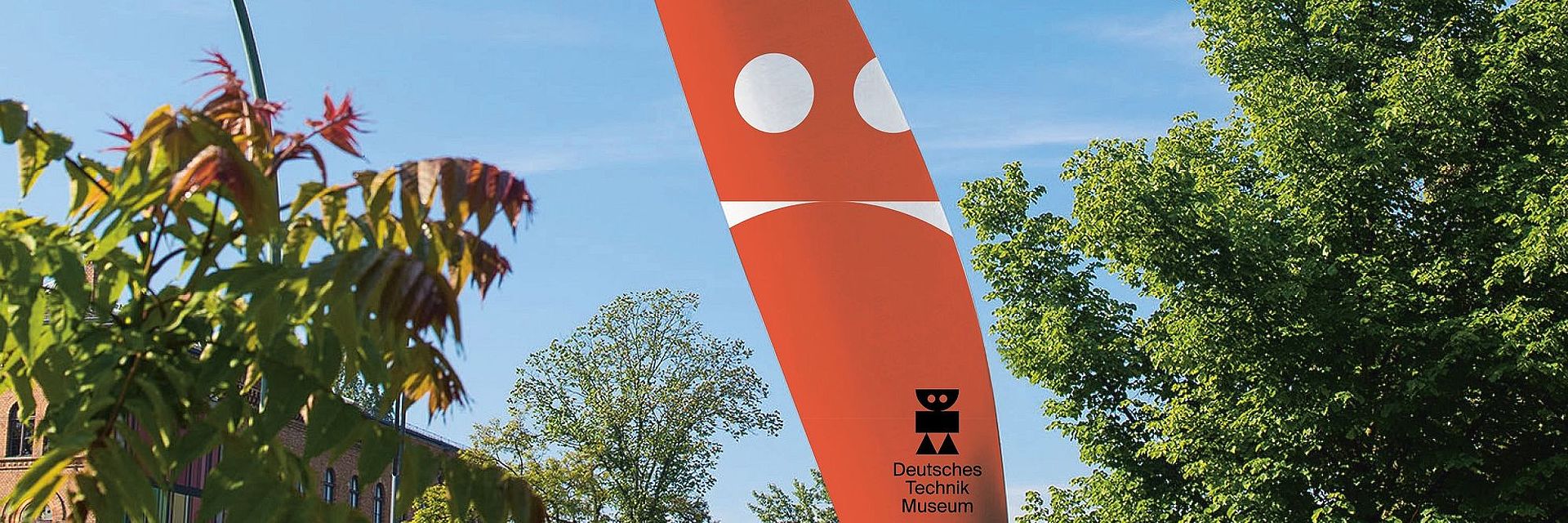 Blick auf das Rotorblatt vor dem Museum, darauf in sehr groß der Roboter aus dem Logo in Rot.
