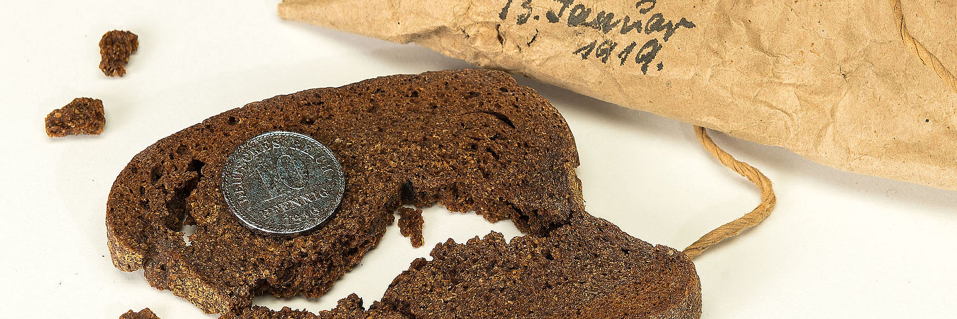 Das Bild zeigt eine hundert Jahre alte Scheibe Brot mit Münze. Das Geldstück wurde vermutlich für eine Hochzeit oder ähnliches eingebacken.