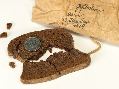 Das Bild zeigt eine hundert Jahre alte Scheibe Brot mit Münze. Das Geldstück wurde vermutlich für eine Hochzeit oder ähnliches eingebacken.