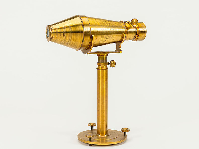 Der Metalltubus dieser Nachbildung der Daguerrotypie-Kamera mit Voigtländeroptik ruht horizontal auf einem Stativ. Sie ist aus poliertem Messing gefertigt.
