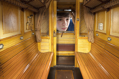 Ein kleiner Junge schaut durch ein Fenster in ein Modell eines Eisenbahnwaggons.