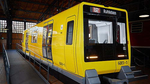 Blick auf das Äußere eines U-Bahnwagens. Der Wagen ist gelb, die Frontpartie schwarz. Der Wagen steht in einem Lokschuppen.