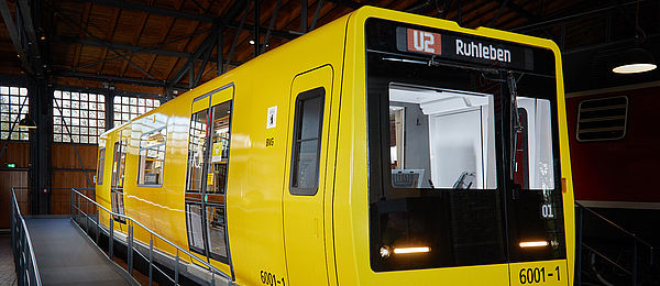Blick auf das Äußere eines U-Bahnwagens. Der Wagen ist gelb, die Frontpartie schwarz. Der Wagen steht in einem Lokschuppen.