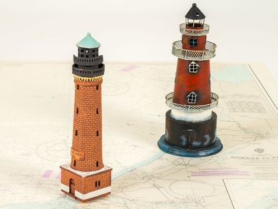 Auf einer Seekarte stehen das Modell eines Leuchtturms aus Backstein und das eines rot-weißen Fantasie-Leuchtturms.
