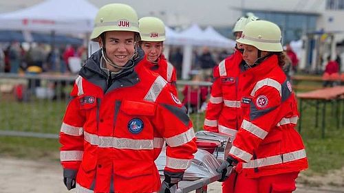 Vier junge Sanitäter und Sanitäterinnen tragen auf einer Veranstaltung eine Transportliege..