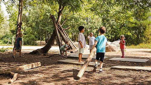 Eine Gruppe Kinder baut in einem Wald etwas aus Holz.