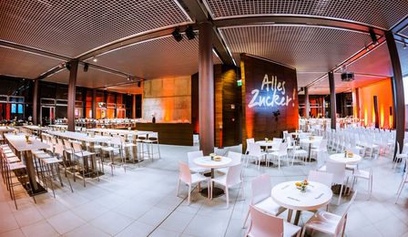Die Eventfläche AUSGUCK ist mit einer gemischten Bestuhlung für eine Abendveranstaltung ausgestattet und festlich orange-blau beleuchtet.