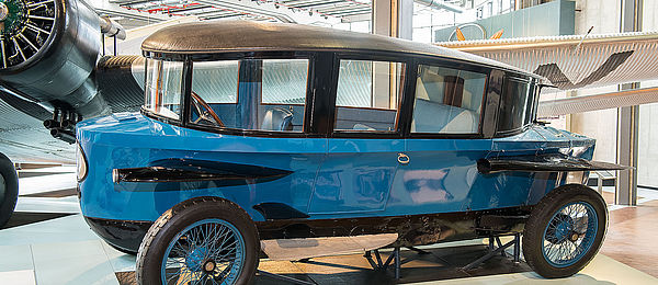 An oblong, blue historical car noteworthy for its aerodynamic raindrop shape. The roof slopes towards the back. The headlights and fenders on the sides are reminiscent of airplane wings.