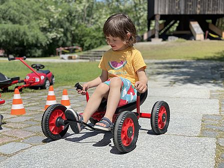 In the Museum Park a girl is riding a red three-wheel-vehicle.